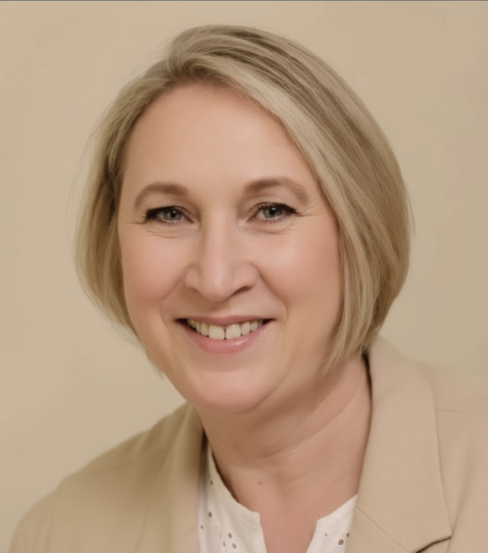 Woman with blonde hair wearing a beige jacket and white shirt against a plain background