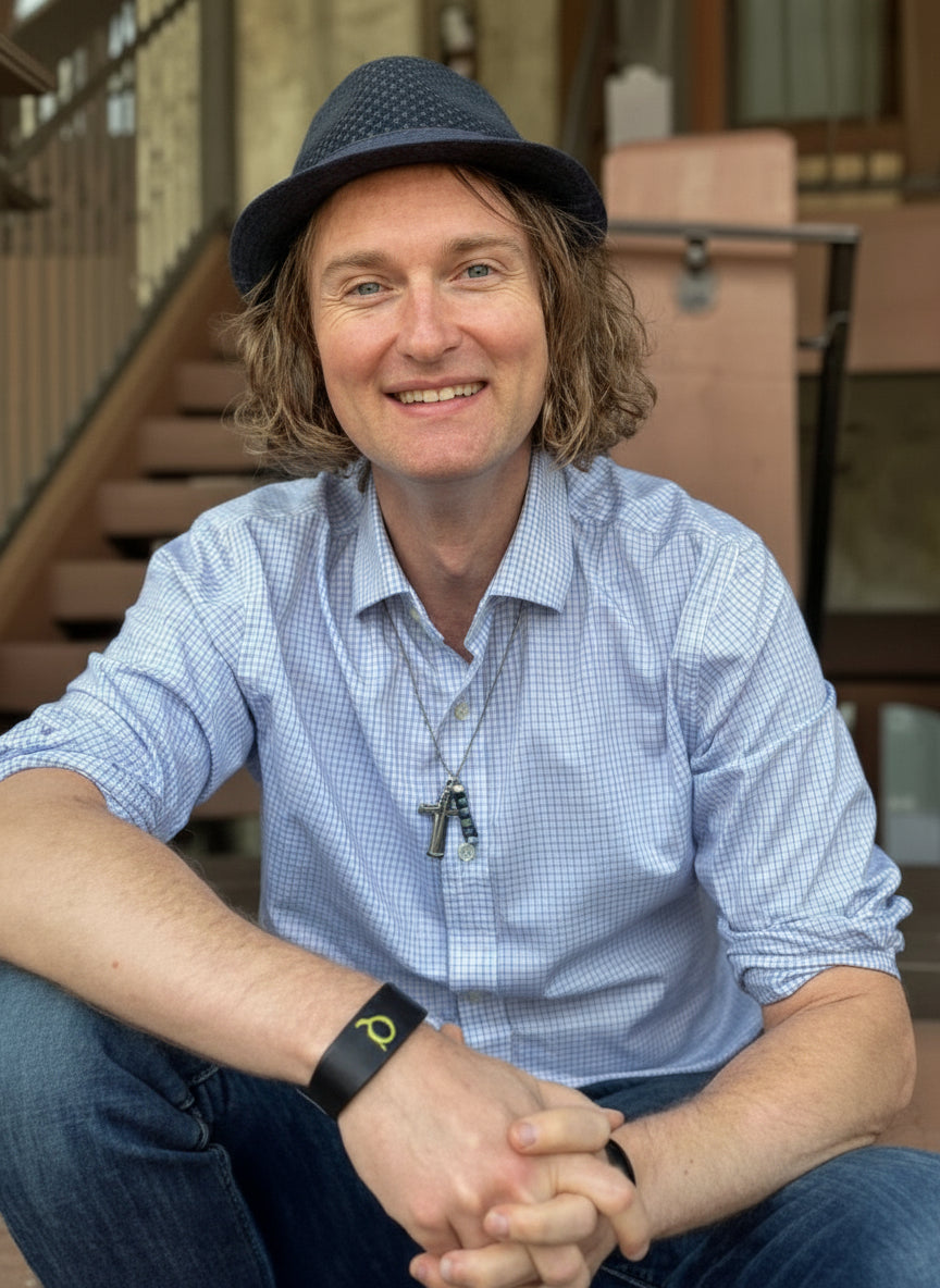 Man wearing a blue checkered shirt and navy hat sitting outdoors.
